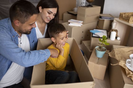 Un couple de parents avec leur petit garçon assis dans un carton en phase de déménagement